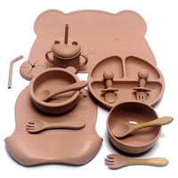Ensemble repas complet en silicone – Édition Ourson, comprenant 10 pièces en silicone sans BPA : assiette compartimentée, bols, gobelet à paille, couverts bois‑silicone et tapis en forme d’ourson, le tout dans une teinte douce et chaleureuse.