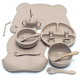 Ensemble repas complet en silicone – Édition Ourson, comprenant 10 pièces en silicone sans BPA : assiette compartimentée, bols, gobelet à paille, couverts bois‑silicone et tapis en forme d’ourson, le tout dans une teinte douce et chaleureuse.